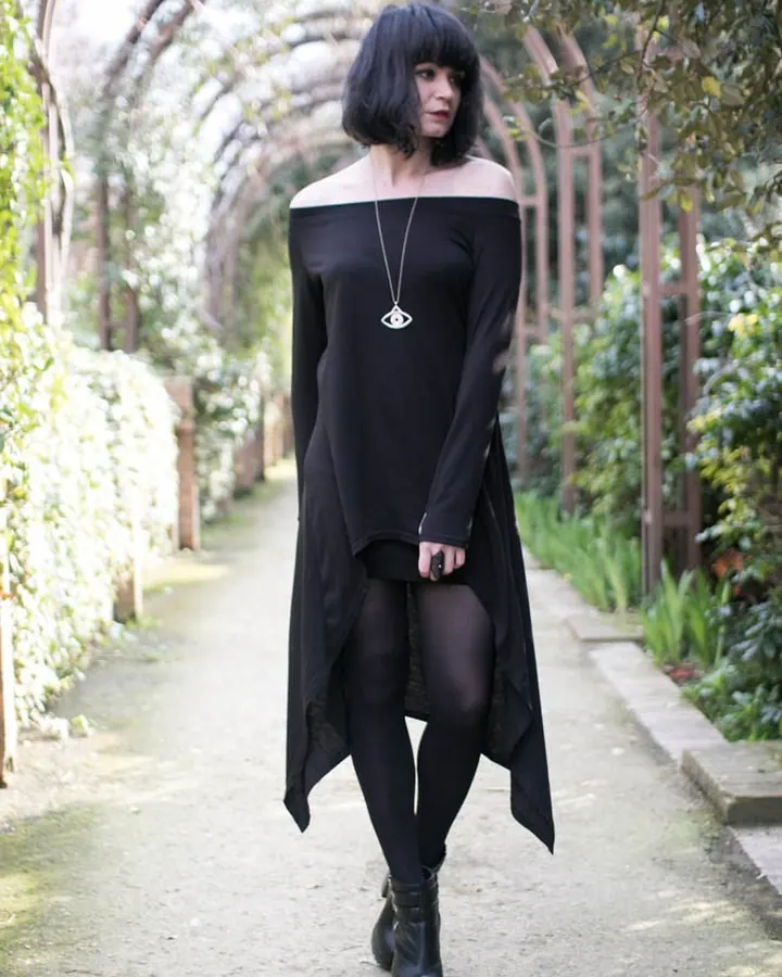Femme aux cheveux bruns-noirs, peau blanche, yeux gris, en robe noire, debout sur un pont au crépuscule, mains sur les hanches.