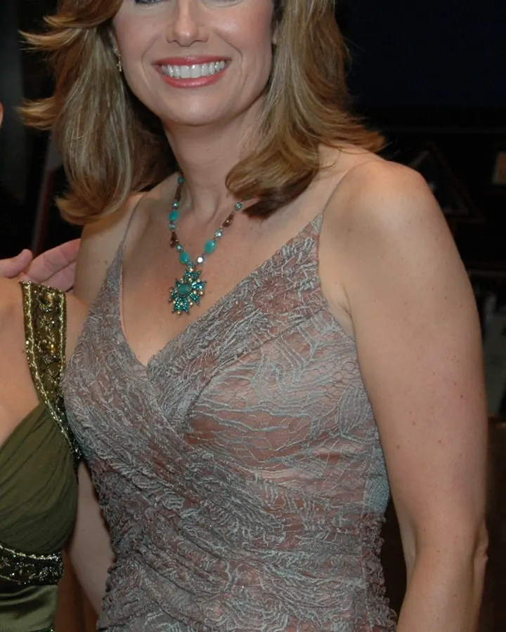 Femme aux cheveux bruns clairs, portant une robe transparente gris argenté, souriant à l'appareil photo.