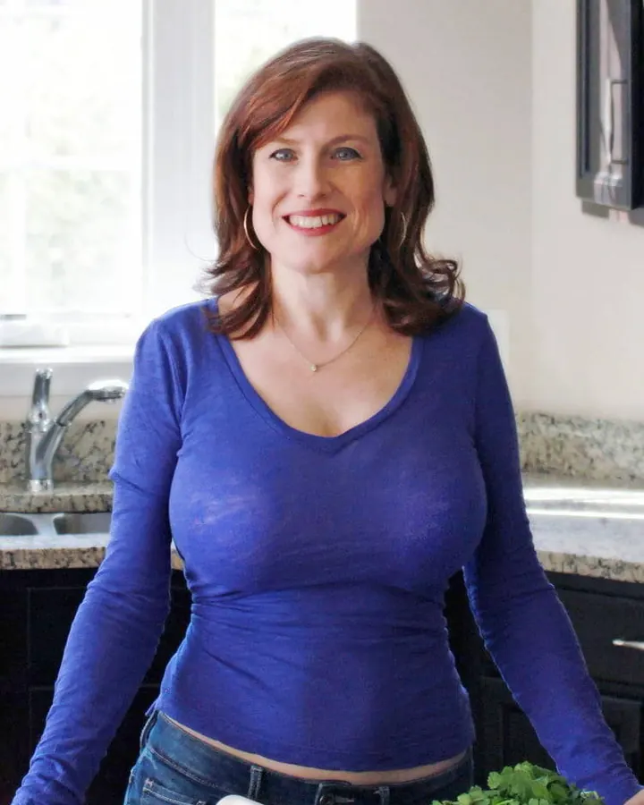 Femme en haut bleu, jeans, souriante dans cuisine
