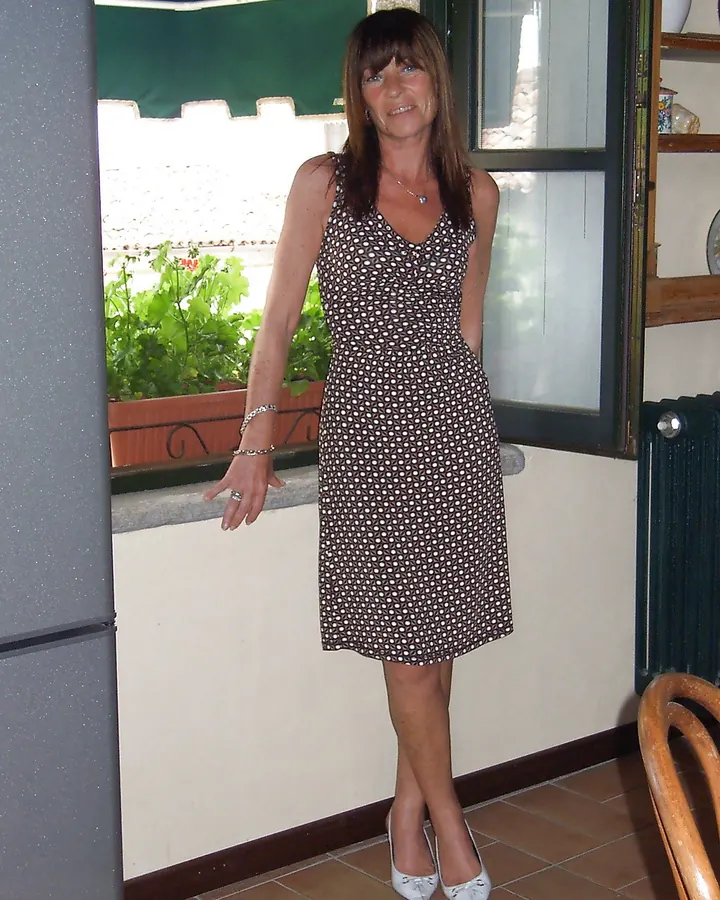 Femme aux cheveux châtains portant un haut blanc et un short en jean, debout devant un armoire blanche dans une chambre rose.