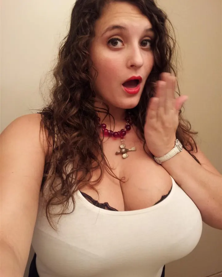 Femme aux cheveux foncés portant un haut blanc, regardant l'appareil photo avec une expression surprise.