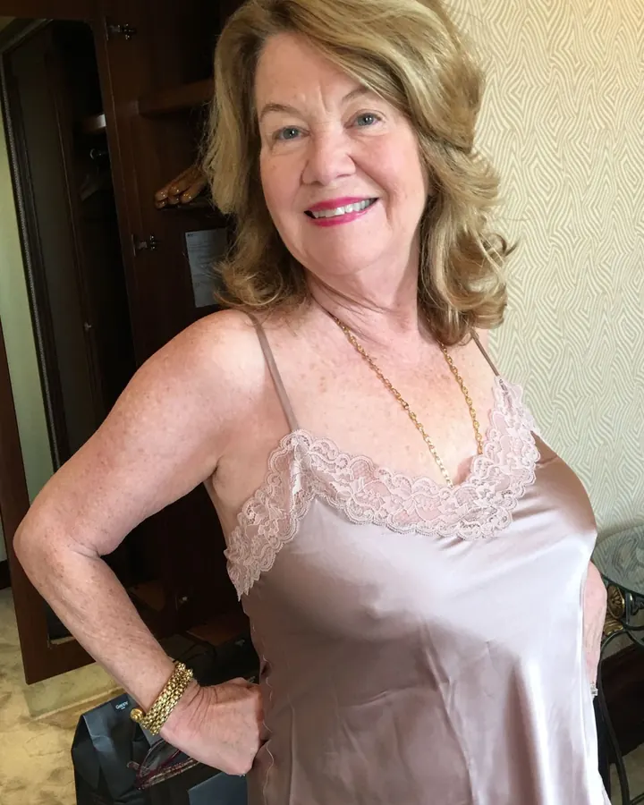 Femme aux cheveux blonds, souriante, en haut rose satiné avec dentelle, en intérieur
