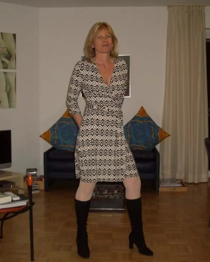 Femme aux cheveux blonds, souriante, en haut noir, debout dans une pièce